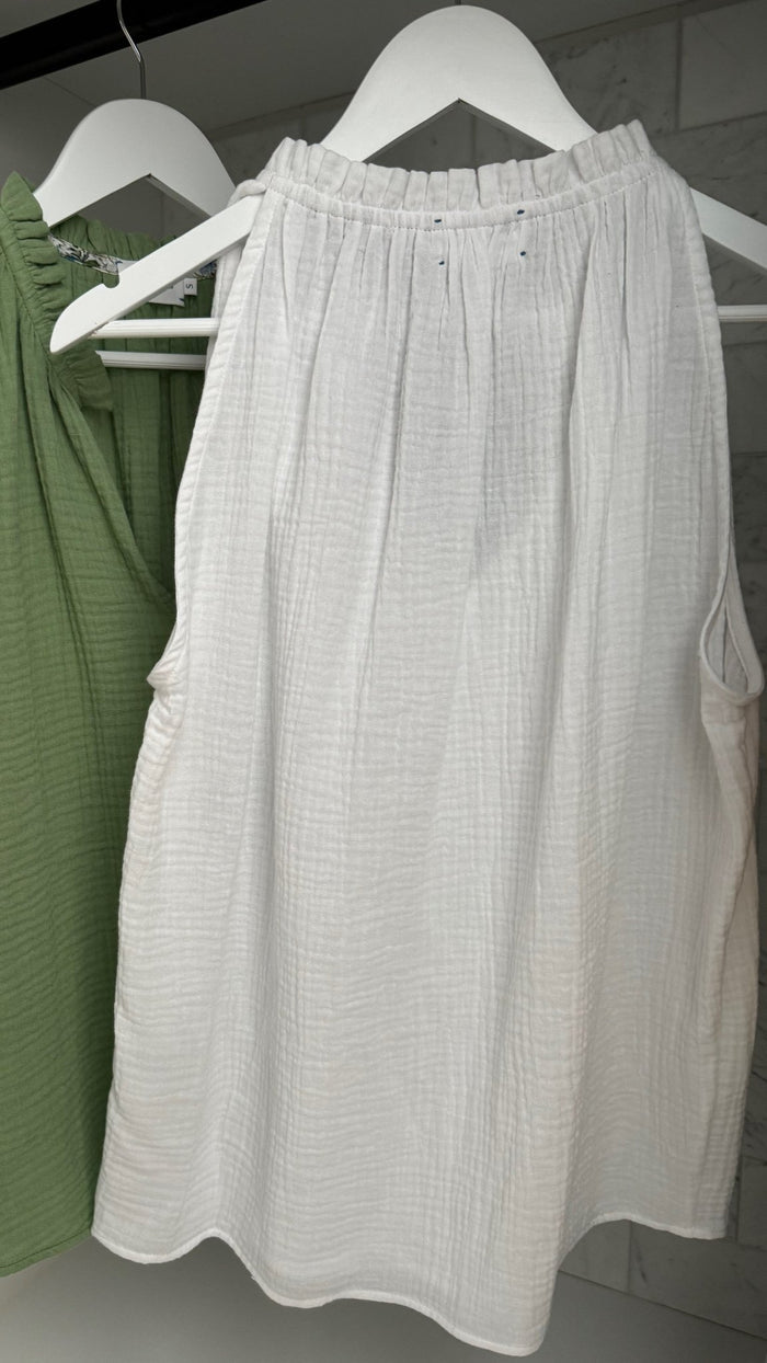 Back of a white sleeveless top and front of a green top with frill around neckline hanging on white hangers - ANNIE.G