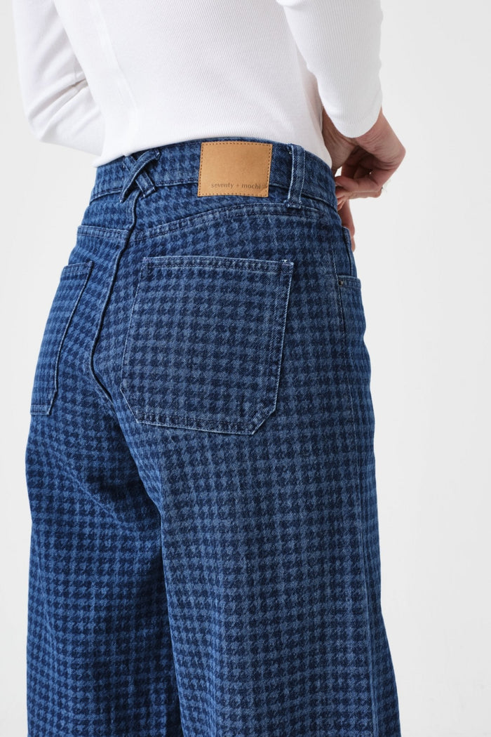 Side of a person wearing blue checkered pants with pockets and belt loops and a white long sleeve shirt.