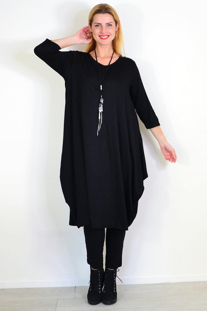 Black relaxed oversized tunic dress by Lilia Whispers hanging on a wooden hanger, showing its loose fit and soft fabric.
