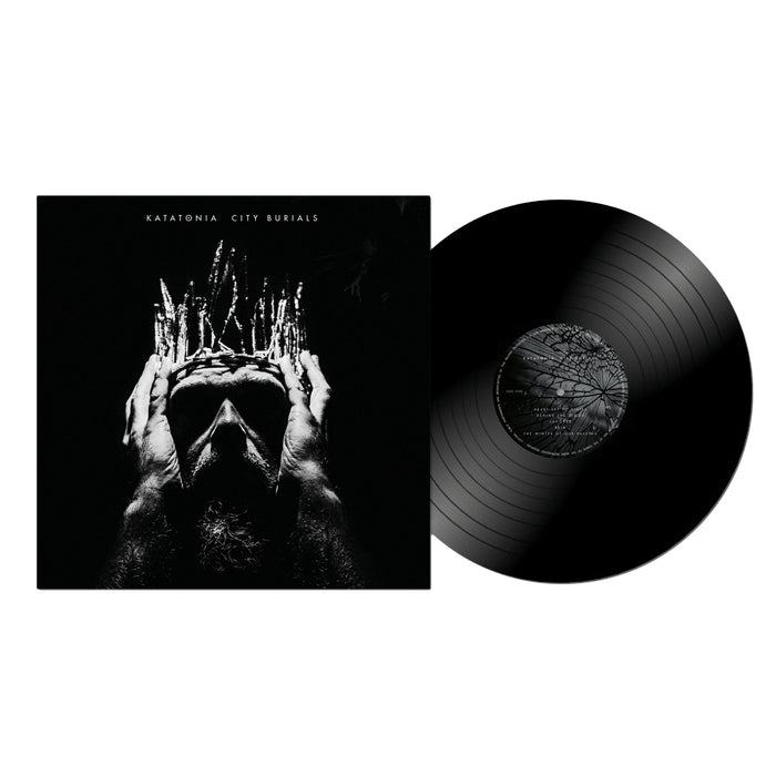 A black vinyl record emerges from its album cover, which displays a grayscale image of a person holding a jagged crown. The cover is topped with the progressive rock album title "City Burials" by Katatonia.
