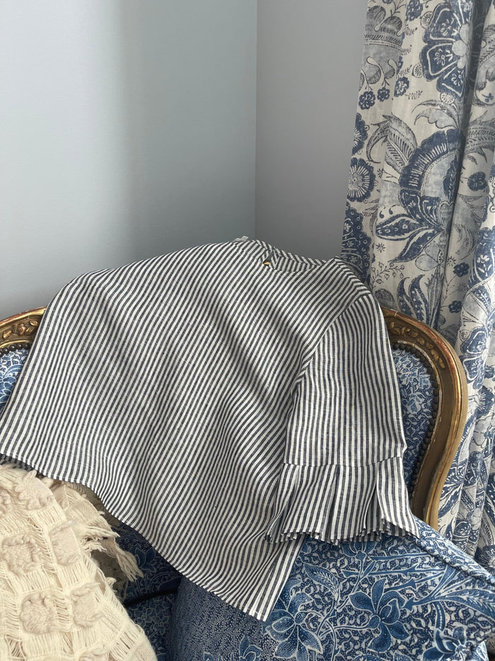 Blue and white stripe woman's top with sleeve pleats at elbow placed over a blue chair.