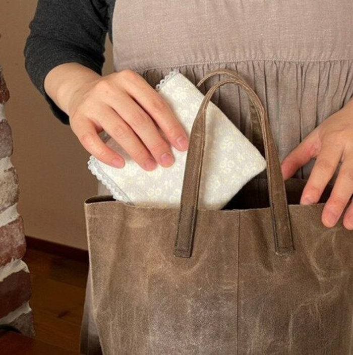 Person placing a folded grey floral face towel in a brown handbag.