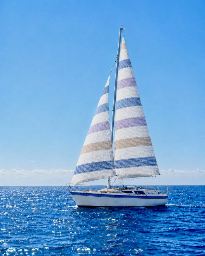 Sailboat with striped sails on a clear blue sky and ocean