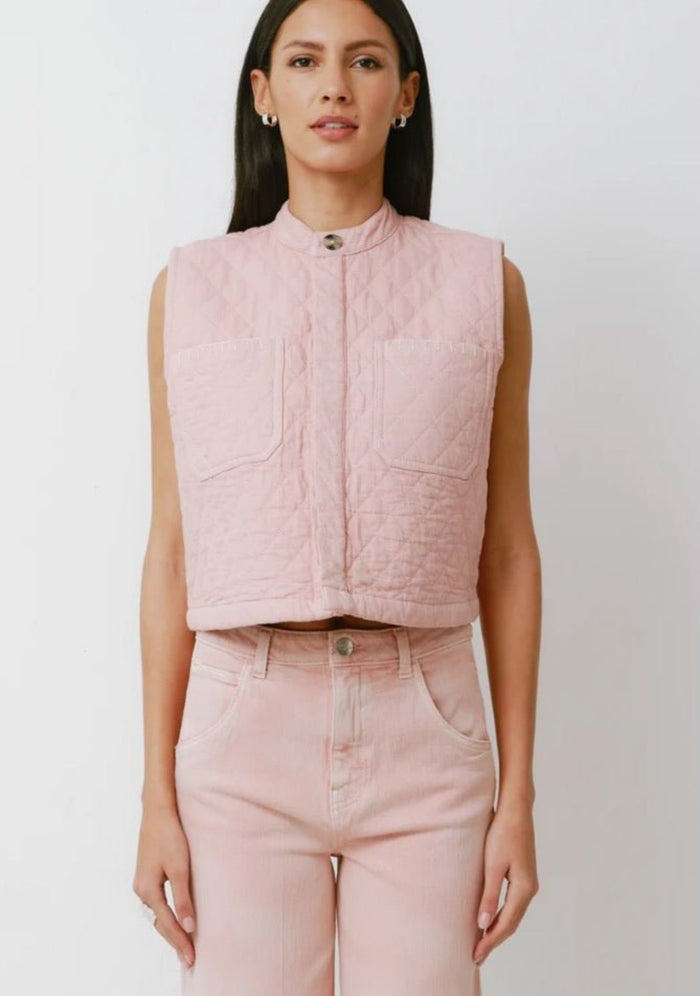 Woman wearing a pink quilted vest buttoned up and pink jeans.