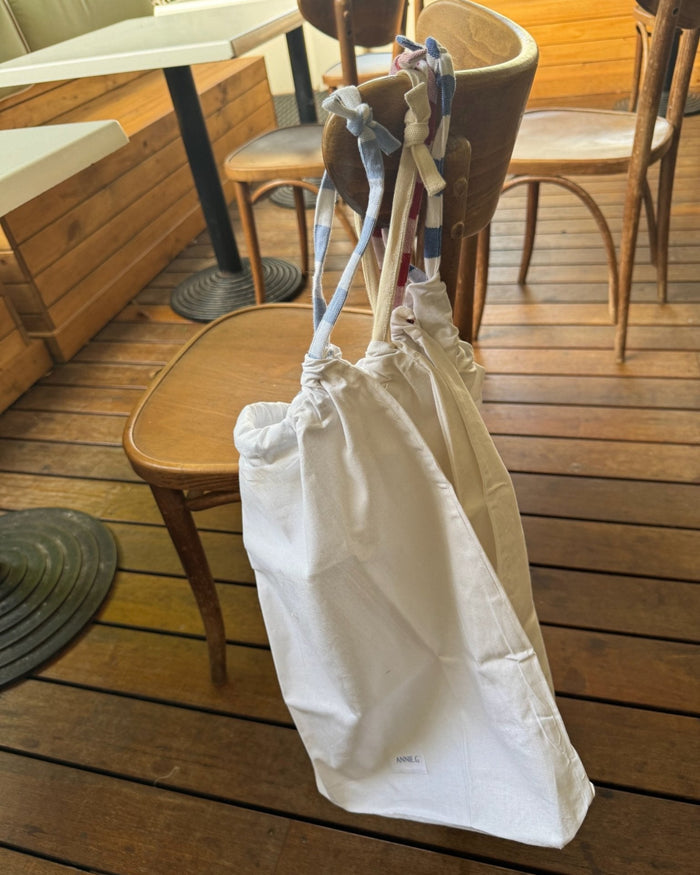 Natural cotton coloured tablecloth storage bag with drawstring closure hanging on the back of a wooden chair.