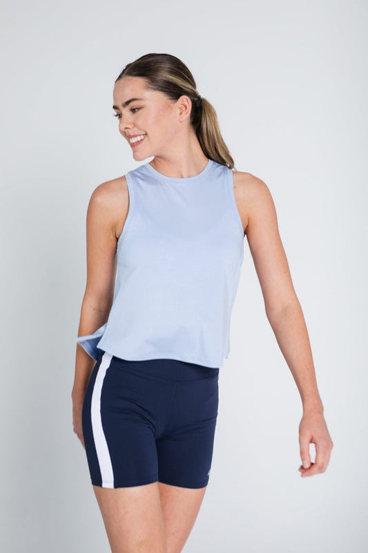 Woman walking and wearing blue tank top with a high low hem and navy bike shorts.