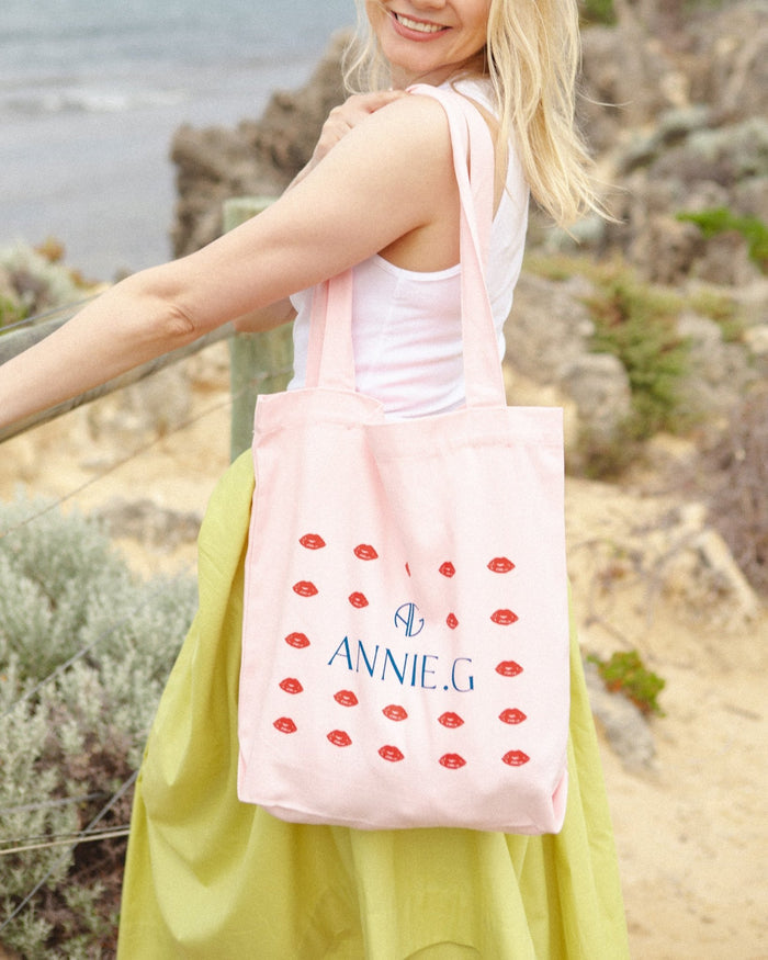 Woman wearing a cotton canvas tote in pink on shoulder with lips screen print design and ANNIE.G branding logo.