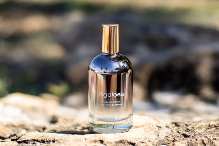 Bottle of 'Ageless Essence' on a rock with a blurred natural background