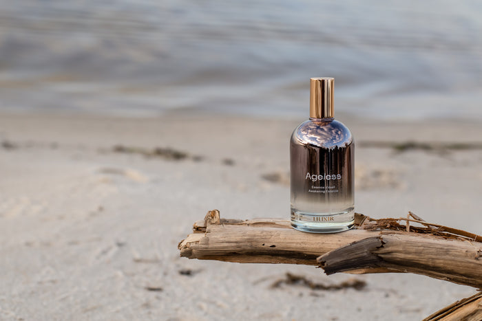 A bottle of Ageless essence on a piece of driftwood by the beach