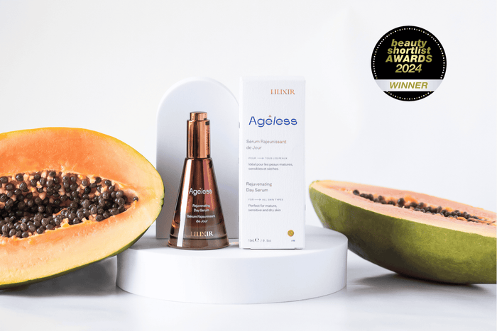 A bottle of LILIXIR Ageless Rejuvenating Day Serum with a background featuring a halved papaya, showcasing the product's natural ingredients. The product is presented on a pedestal with an award badge description in the top right corner.