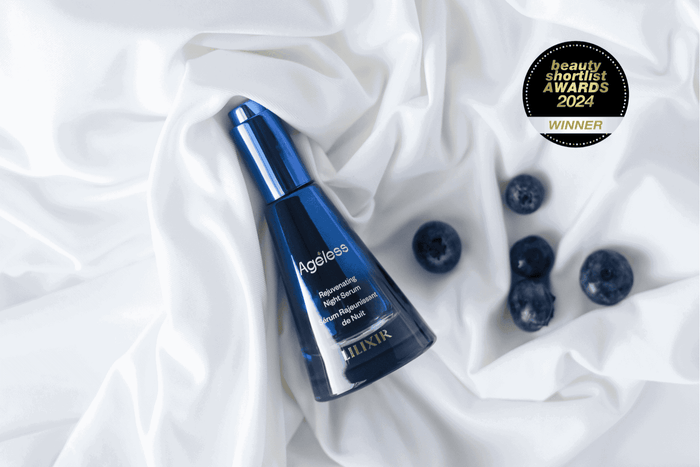 Blue skincare serum bottle labeled 'lilixir Ageless' on white fabric with blueberries, and a 'Beauty Award Winner' badge.