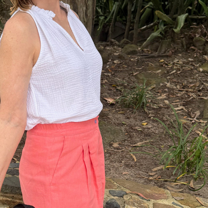 Woman wearing a white cotton gauze tank with split neckline and ruffle detail with strawberry coloured shorts - ANNIE.G