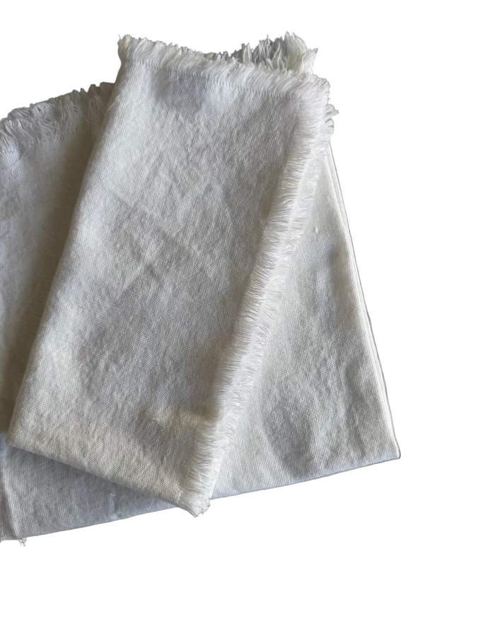 One white fabric napkin with a frayed edge folded on top of another white napkin
