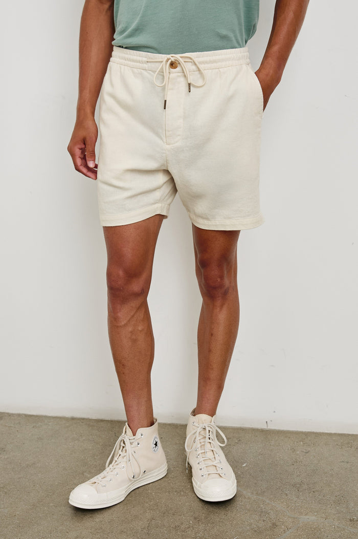 Archer medium length cotton short with adjustable drawstring and front button closure in Ecru - front view on model, hand in pocket