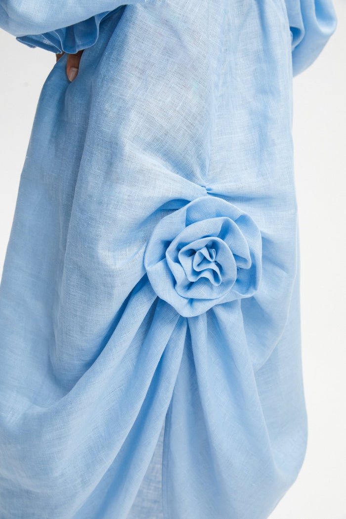 Rosette detail on a woman's blue linen dress creating a front split.