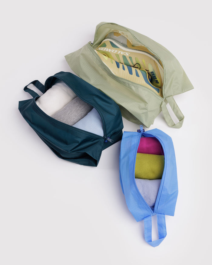 Three colourful packing cubes with zips open and clothes and shoes inside