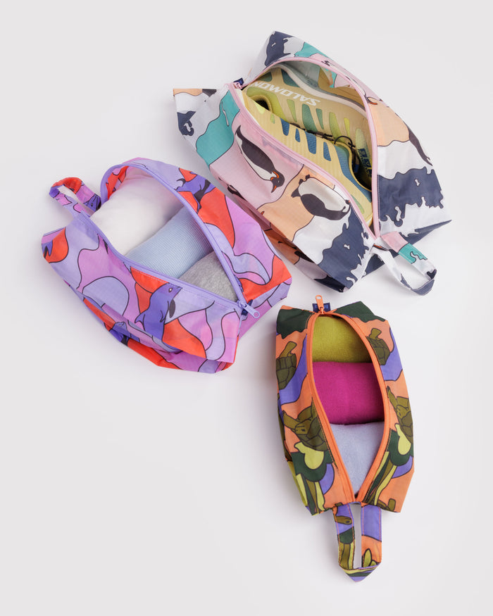 Three colourful animal print fabric bags with zips open and clothes and shoes items inside.