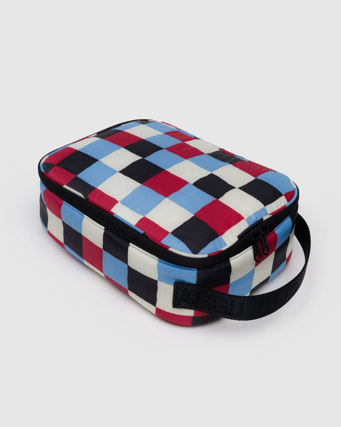 Baggu lunch box in checkered pattern of white, blue, burgundy and black squares with black webbed handle and zip fastening.