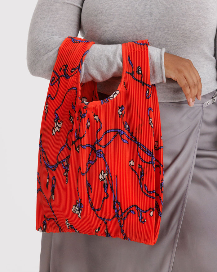 Person holding a red pleated bag with blue floral patterns.