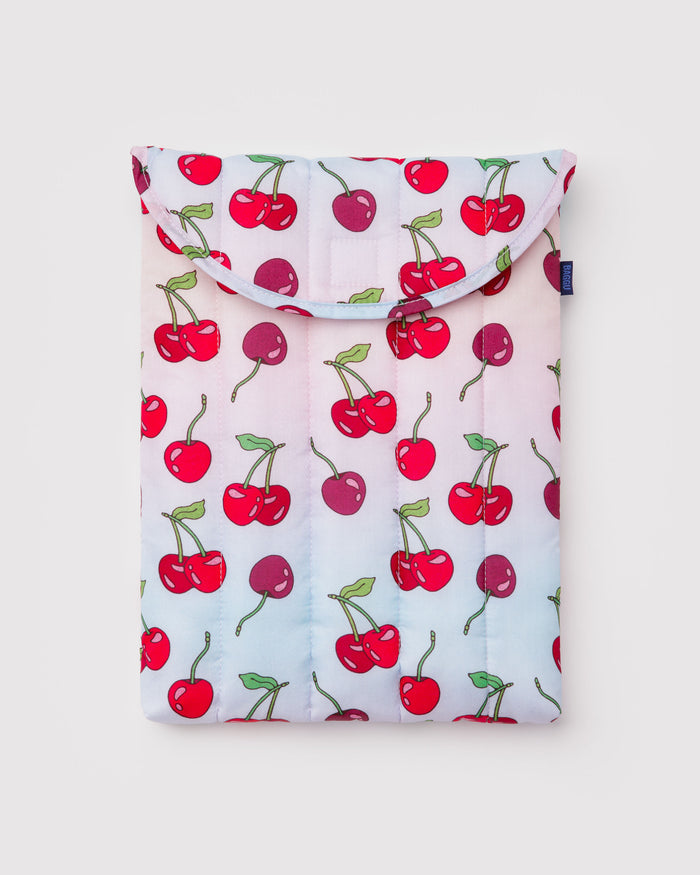Pink and blue quilted and puffy laptop sleeve with cherries pattern and BAGGU logo tag at the side.
