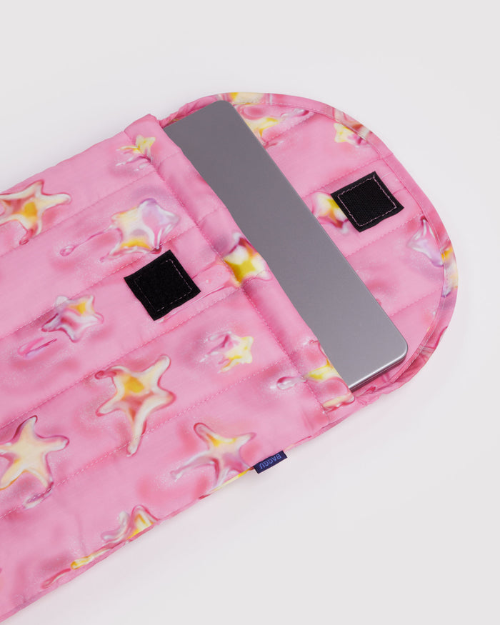 Quilted and puffy pink laptop sleeve with yellow star pattern and a silver laptop inside and velcro closure.