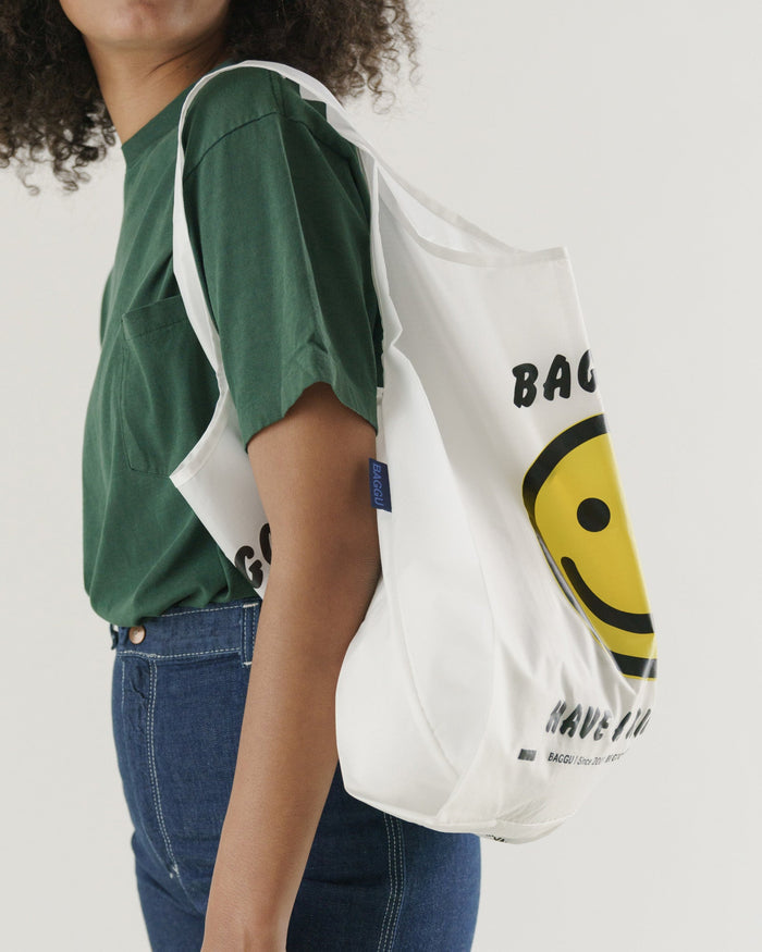Person wearing a green shirt and blue jeans with a white tote bag featuring a smiley face design.