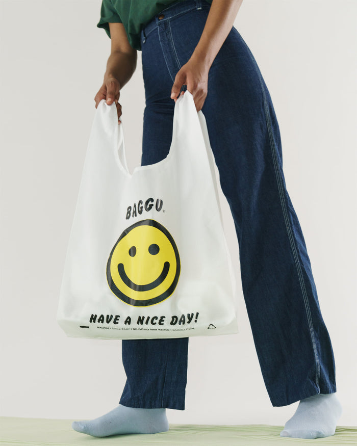 Person holding a white reusable bag with a smiley face design and text.