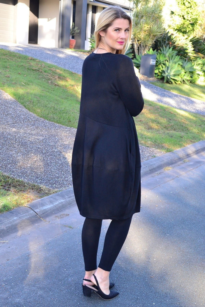 Black Peony Cocoon Winter Pocket Tunic Dress hanging on a hanger, showing its cozy, relaxed fit with front pockets and long sleeves.