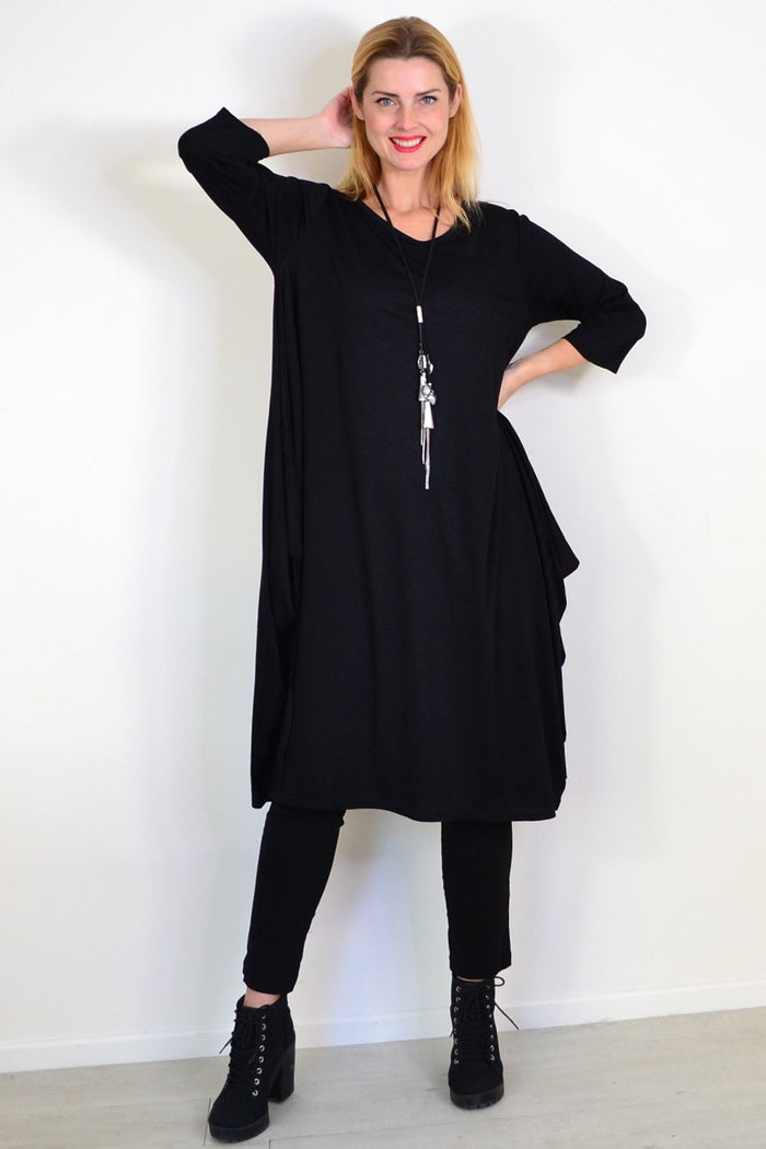 Black Lilia Whispers relaxed oversized tunic dress hanging on a wooden hanger with a soft background.