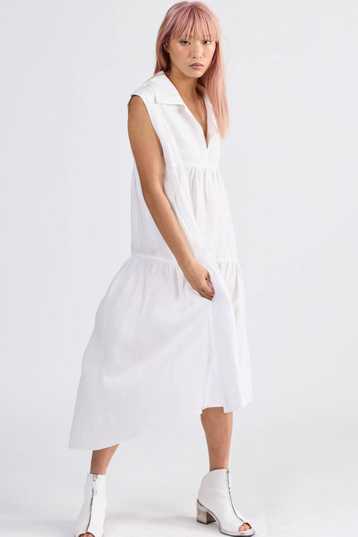 Side of woman wearing a sleeveless ivory dress with v neckline and dropped hem at back - ANNIE.G