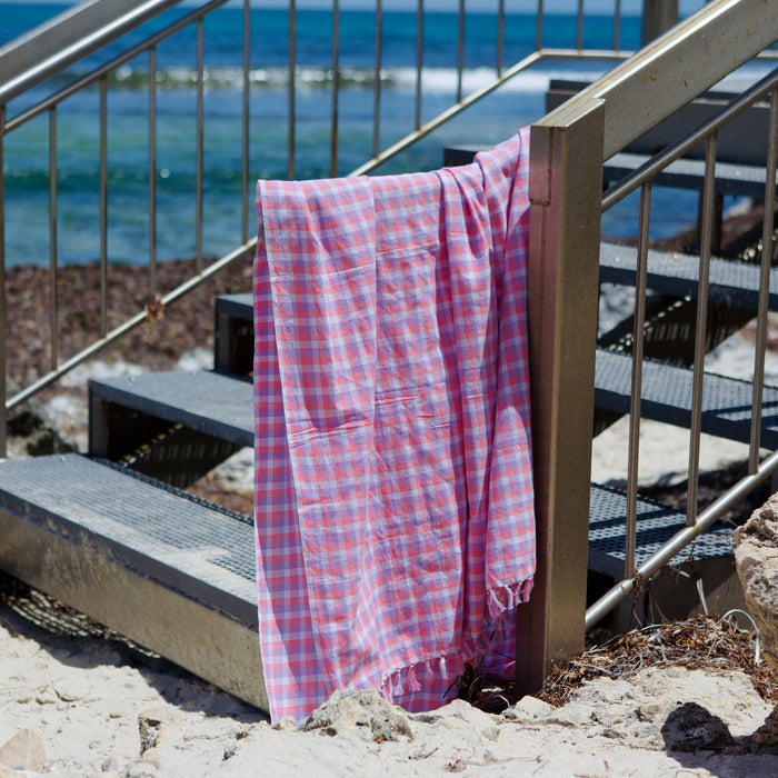 pink checked cotton beach towel with fringe over rail at beach - ANNIE.G