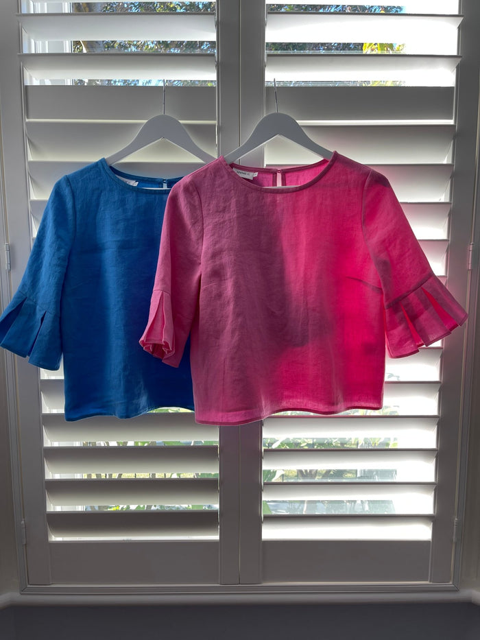 Blue and a pink round neck top and button keyhole at back hanging on shutters inside.