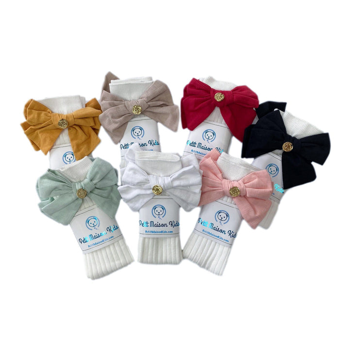 Ribbed cotton girls socks with large linen bow and gold logo detail, soft breathable design available in multiple colors.