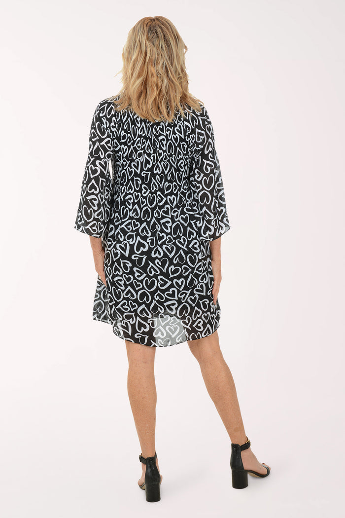A woman wearing a black and white 3/4 sleeve dress with a heart pattern.