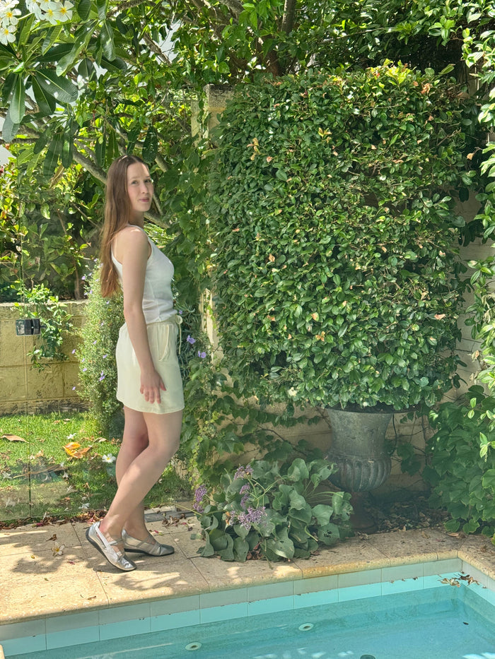 Woman waering honeycomb miskirt 40cm, white tee and sandshoes standing by a pool with greenery in the background.