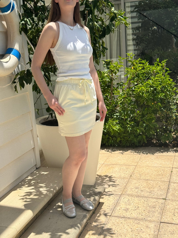 Woman in honeycomb mini skirt and white top standing on a step next to pot plant.