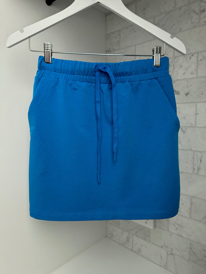 Royal blue miniskirt 40cm length with elastic waist and drawcord and side pockets hanging on a white skirt hanger with tiles on the wall - ANNIE.G
