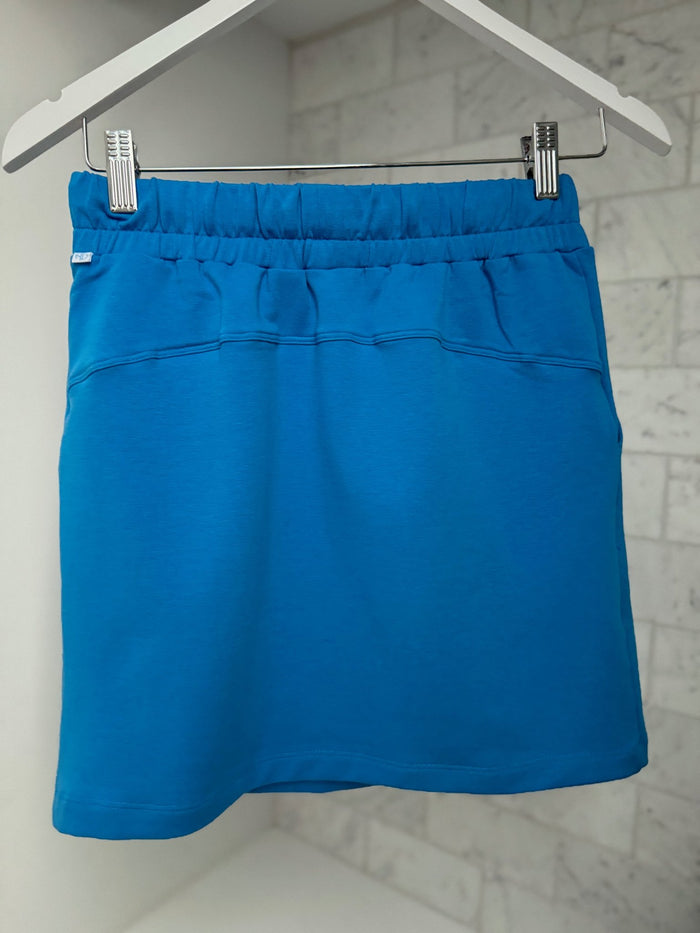 Back of a royal blue miniskirt 40cm length with elastic waist hanging on a white skirt hanger with tiles on the wall - ANNIE.G