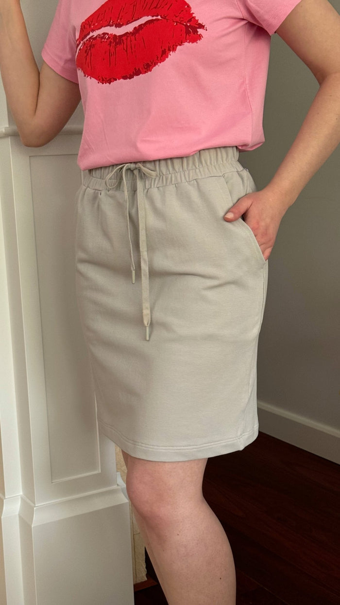 Woman wearing a light grey miniskirt 50cm length, elastic waist and drawcord with hand in side pocket and pink lips t-shirt - ANNIE.G