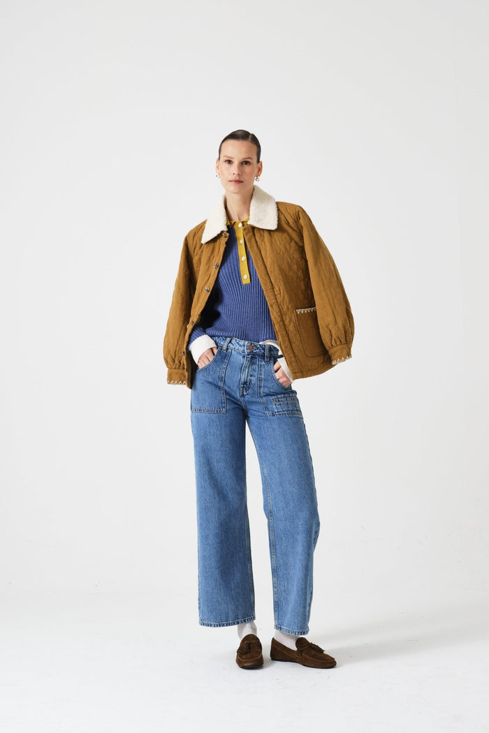 Woman wearing a brown quilted  jacket with a white collar, blue shirt, and jeans