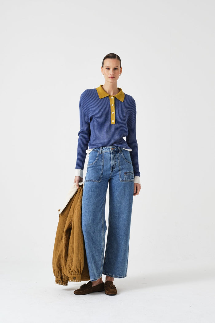 Person wearing a blue sweater with yellow collar and blue jeans, holding a brown jacket