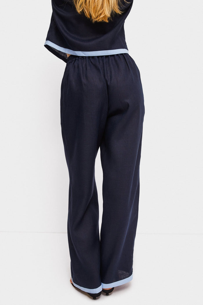 Woman facing the back wearing long navy pants with a light blue contrast hem and matching shirt.