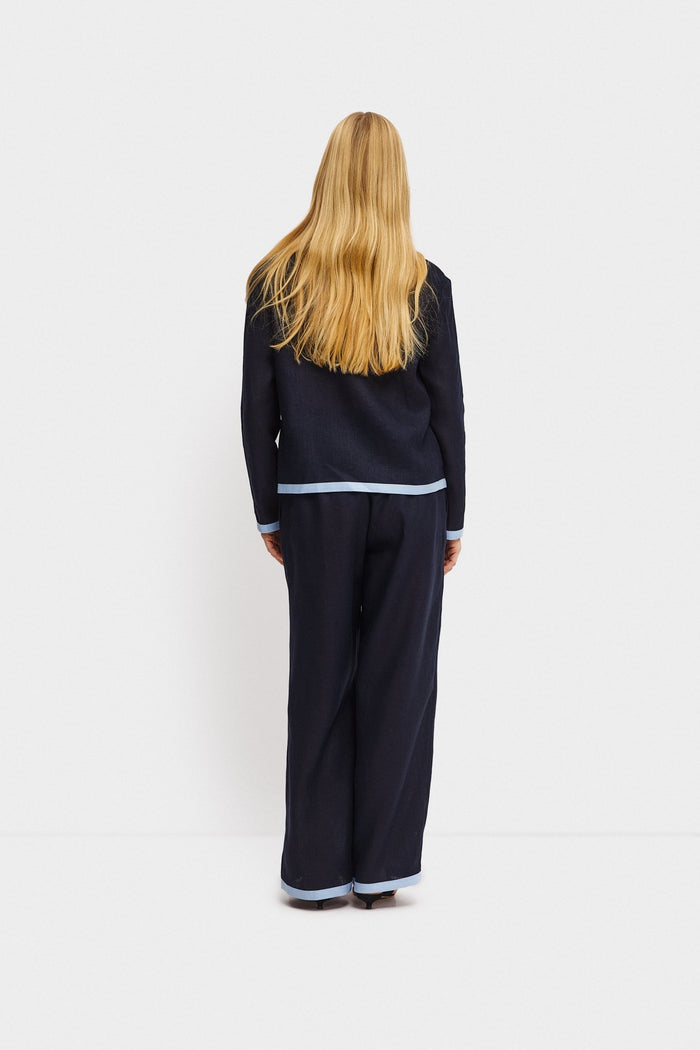 Back of woman wearing long navy pants and matching navy shirt with contrast light blue trim on hem.
