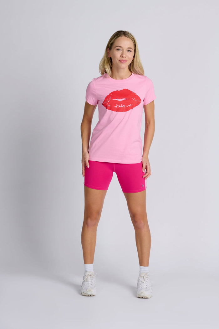 Woman wearing a pink tshirt with red lips graphic and pink bike shorts.