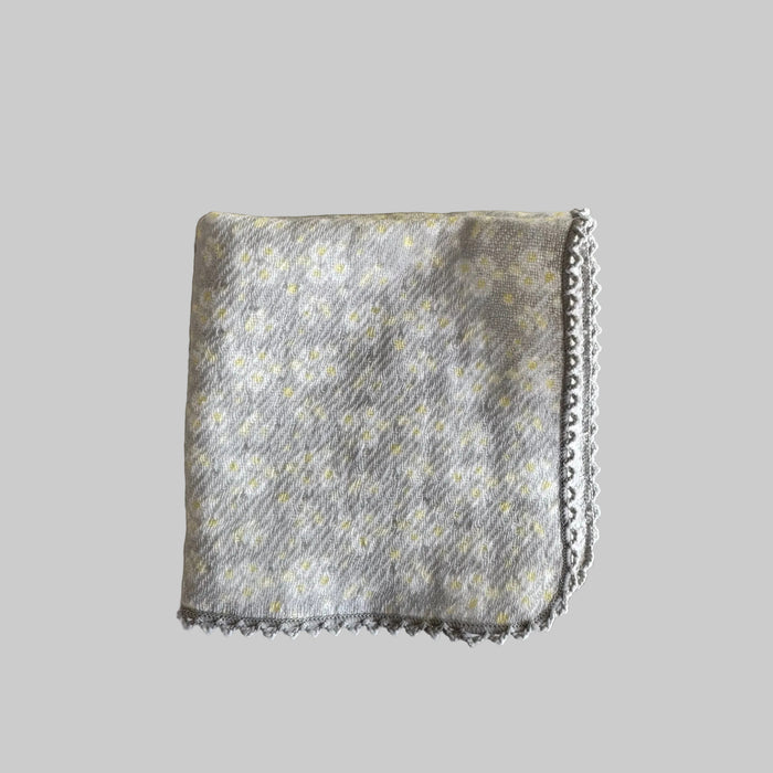 A folded grey with white and yellow flowers print and delicate grey crotchet edge face cloth.
