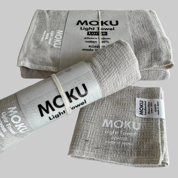 Moku light bath towel set in face washer, hand towel and bath towel in a natural colour each folded with a packaging sleeves and with white writing on fabric.