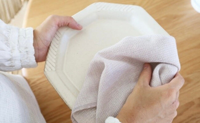 Person wiping a plate with a blueberry coloured towel with a wooden surface in the background.