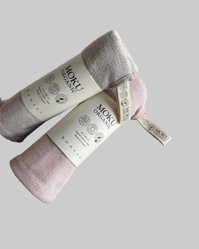 Two Moku organic cotton towels rolled and stacked in pink and blue.