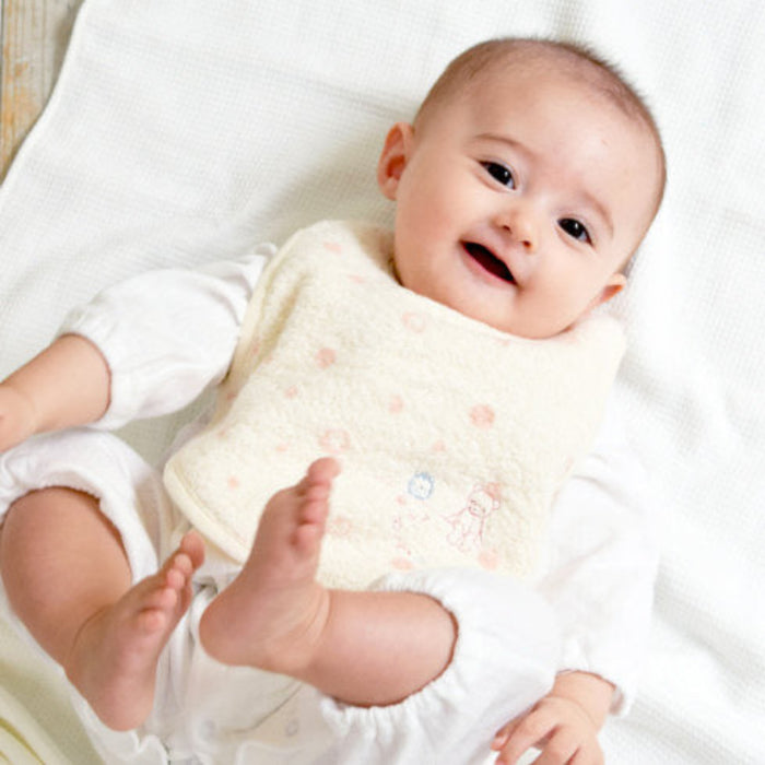 Baby wearing a cream bib with peach pink polka dots and embroidered  teddy.