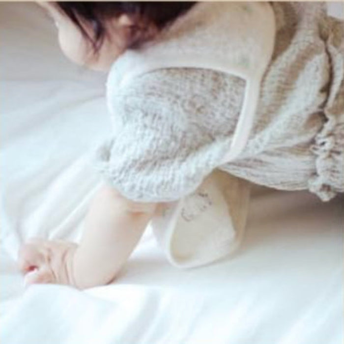 Baby wearing a cream apron bib over short sleeve garment and crawling on white mat.
